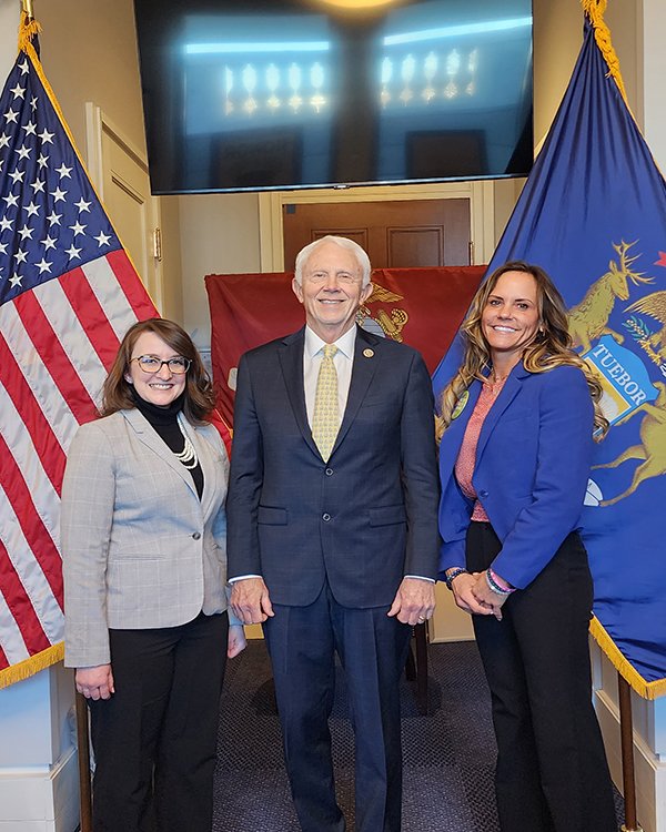 Christine Riley, US Rep., Jack Bergman, and Melissa Dunkle stand together in front of American and Michigan flags.